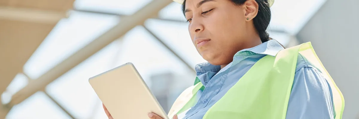 Contractor in a hard hat and hi-vis vest checking a tablet on a job site