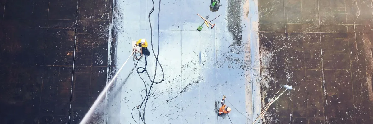 Overhead view of workers in hard hats hydro blasting the floor of a large industrial tank
