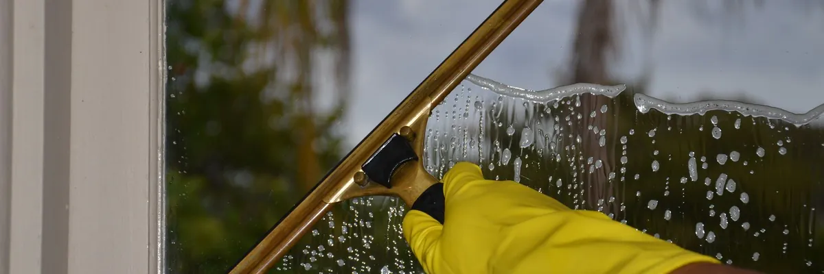 Gloved hand cleaning a window with a squeegee